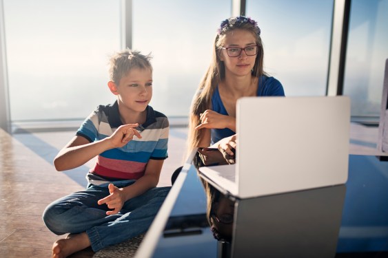 Brother and sister sitting modern apartment and learning sign language online.