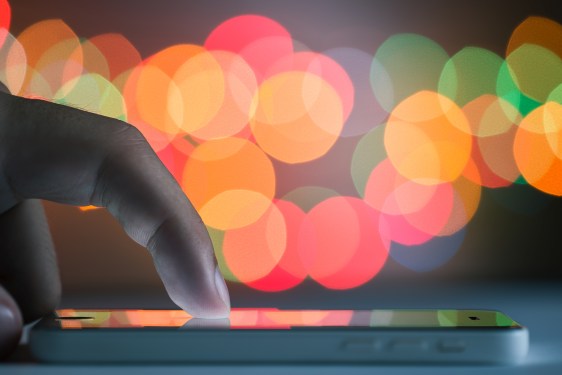 A man uses a smartphone. Close-up shot. Color bokeh in the background.