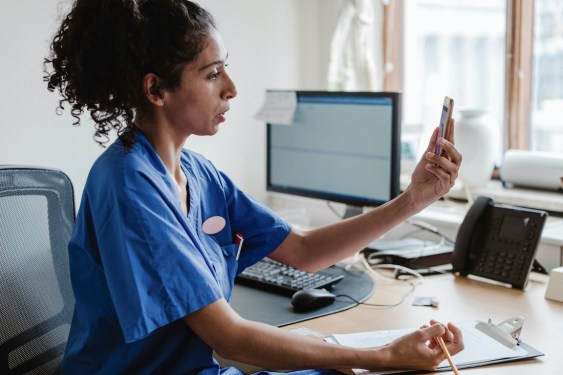 Female healthcare worker talking on video conference through mobile phone in doctor's office