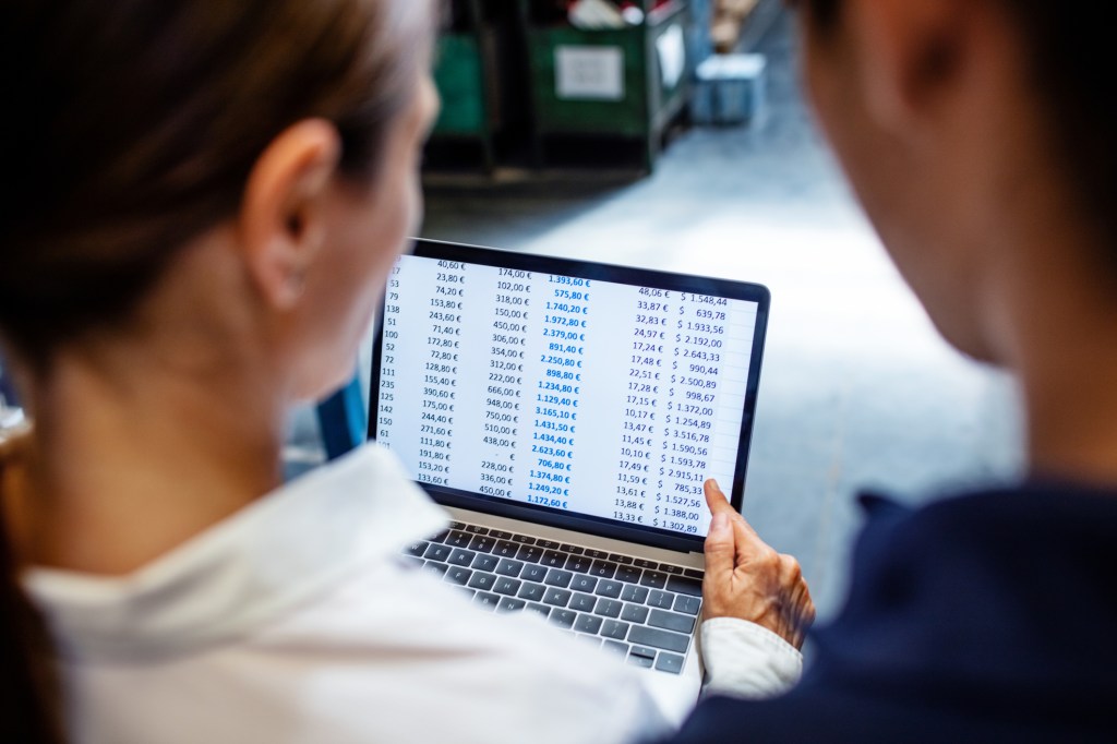 Young woman showing stock level to a worker in warehouse on a laptop computer. Warehouse manager with worker verifying stock level on system.