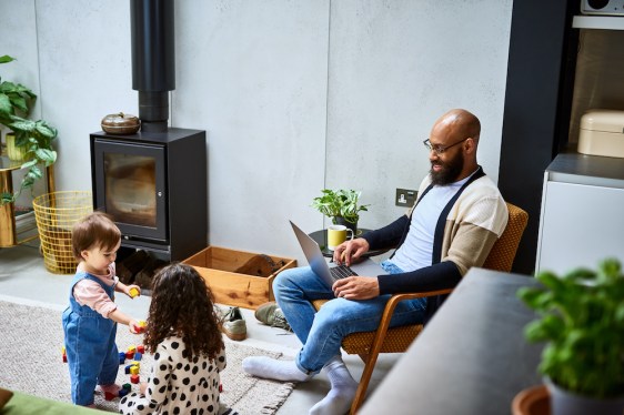 Mid adult man sitting on chair smiling at two daughters playing with blocks, modern life, fatherhood, care, family