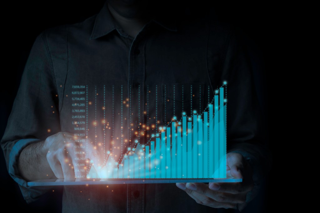 A male businessman is standing by a tablet analyzing the ongoing upwards of the graph. A rapidly changing business concept on a black background.