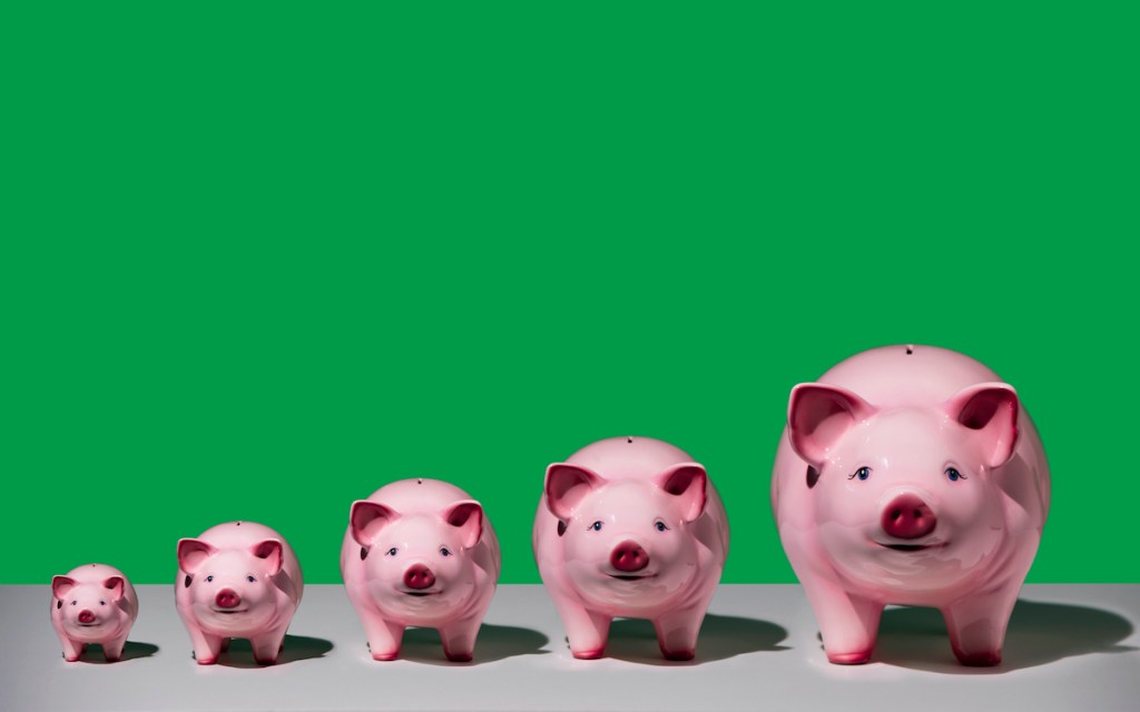 Line of differently sized pink ceramic piggy banks in ascending size order on white surface, green background