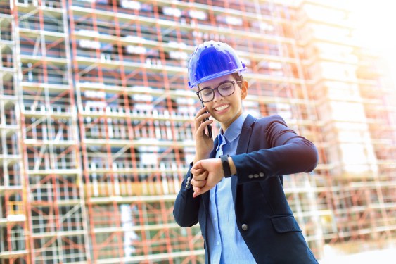 Female architect on a construction site, talking on mobile phone and checking the time. About 25 years old, Caucasian women.
