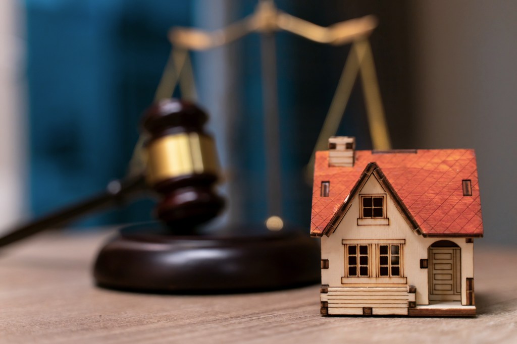 Photo illustration showing a gavel and scales of justice behind a miniature wooden house