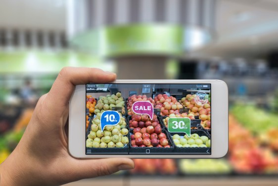 Woman holding a mobile phone using an augmented reality application to check special sale prices of fruits in a grocery. (Woman holding a mobile phone using an augmented reality application to check special sale prices of fruits in a grocery., ASCII,