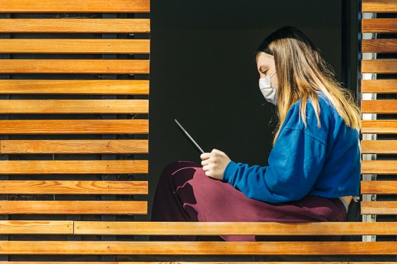 Teenage girl in mask sitting in window of modern house