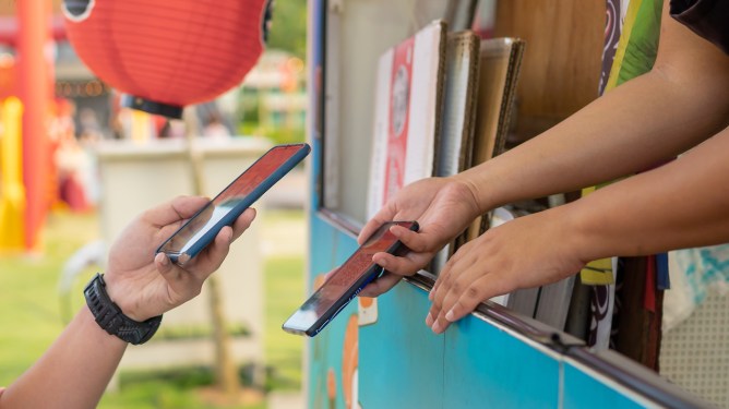 Photo of human hand holding smartphone and scanning the barcode for contactless payment at the food truck.