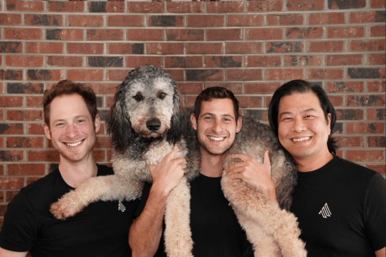 Accord founding team holding their large dog in front of a brick wall background.