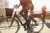 Low section of mature woman riding electric bicycle by commuters on bridge in city against sky