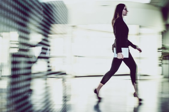Businesswoman Walking Through The Office Corridor and Carrying Tablet