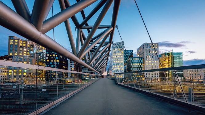 Beautiful twilight over downtown Oslo, the capital city of Norway at Pedestrian Bridge over rails of central railway station. Illuminated modern buildings and skyscapers. Cityscape from elevated walkway in late summer. Oslo, Norway, Scandinavia