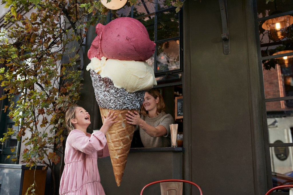 Cheerful girl buying large ice cream cone from take out counter of cafe