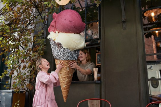 Cheerful girl buying large ice cream cone from take out counter of cafe