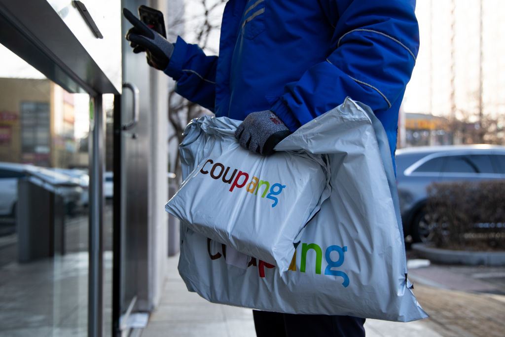 A Coupang Corp. employee holds packages in front of an apartment building in Bucheon, South Korea, on Friday, Feb. 19, 2021