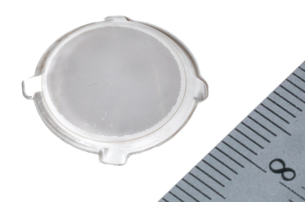 A contact lens with many tiny photovoltaic dots on it next to a ruler showing it is less than a centimeter wide.