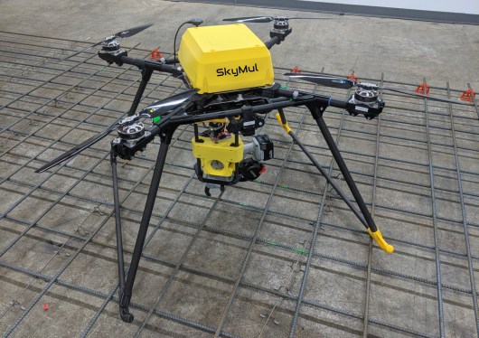 A yellow SkyMul drone with a rebar tying tool sitting on top of some rebar