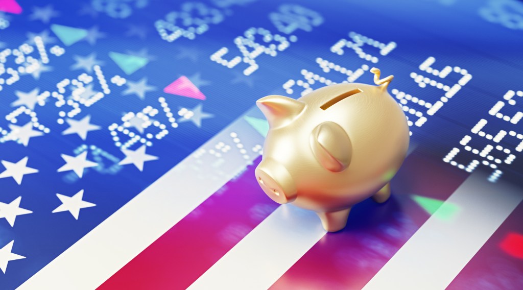 Gold colored piggy bank sitting over American flag and blue financial bar graph. Selective focus. Horizontal composition with copy space. American stock market and finance concept.