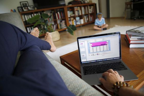 A man works on an Apple Inc. MacBook Pro laptop computer in the lounge of a home as a child wearing headphones sits beyond in this arranged photograph taken in Bern, Switzerland, on Wednesday, Aug. 19, 2020. The biggest Wall Street firms are navigating how and when to bring employees safely back to office buildings in global financial hubs, after lockdowns to address the Covid-19 pandemic forced them to do their jobs remotely for months. Photographer: Stefan Wermuth/Bloomberg via Getty Images