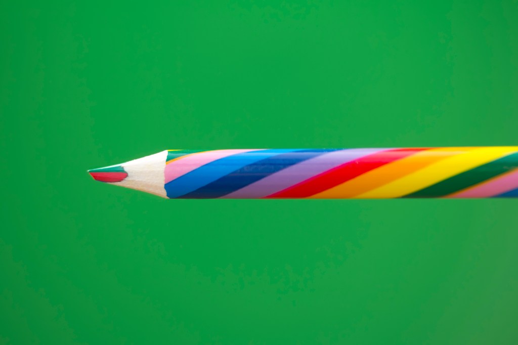 Image of a multicolored pencil on a green background.