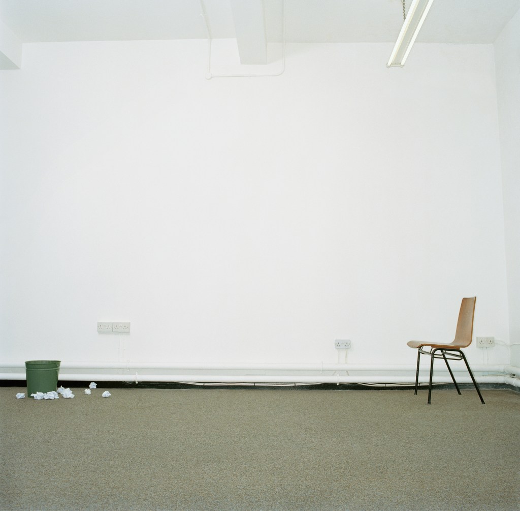 Image of a chair and a trash can in an office, with the bin surrounded by crumpled paper, representing persistence.