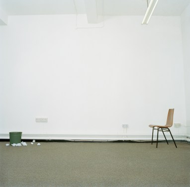 Image of a chair and a trash can in an office, with the bin surrounded by crumpled paper, representing persistence.