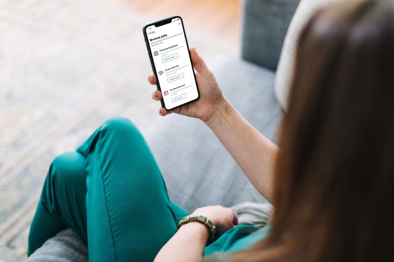 A photo of a person wearing healthcare scrubs holding a smartphone with the Vivian Health jobs app displayed