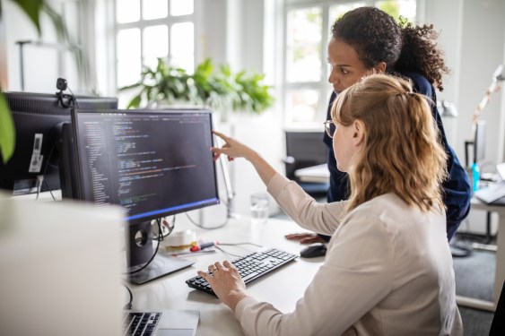 Businesswoman discussing computer program with female colleague at desk in creative office