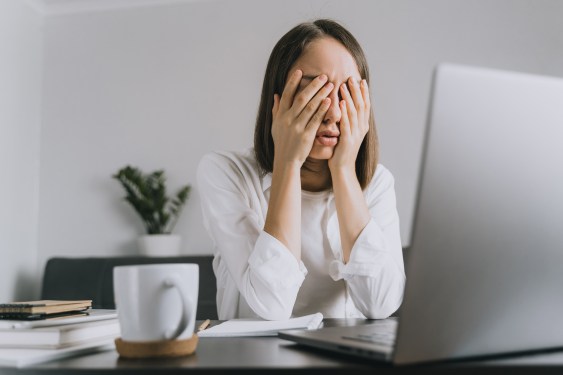 Image of a woman sitting in front of a laptop with her head in her hands.