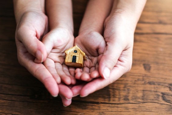 Photo of an adult and child's hands cradling a small wooden house