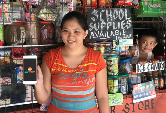 A photo of a sari sari store owner holding a smartphone with the GrowSari app open