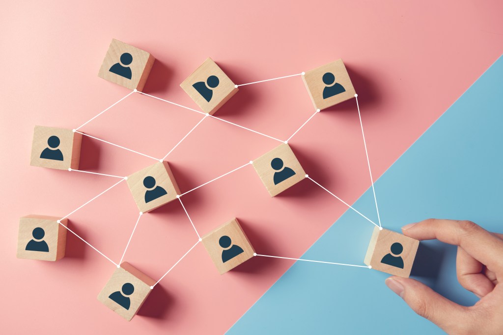 Image of wooden blocks with people on them on a pink and blue background to represent gaining more users via accessibility.