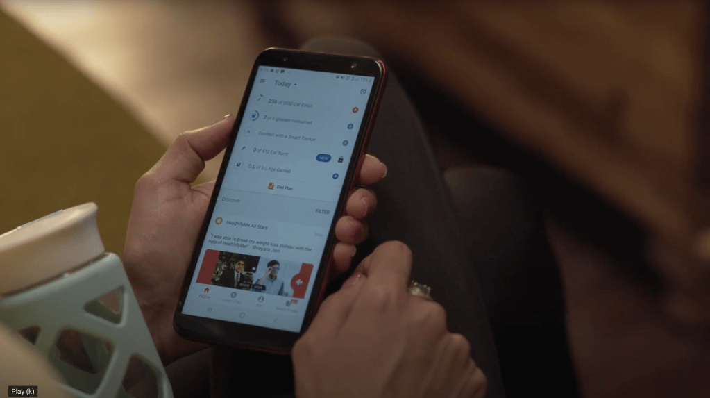 Photo of a person holding a water bottle and smartphone open to HealthifyMe app