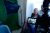 A woman is sitting in front of a video camera and some lighting gear.
