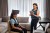 A man wears a BrainQ headset while sitting in a chair, while a woman operates a tablet near him.