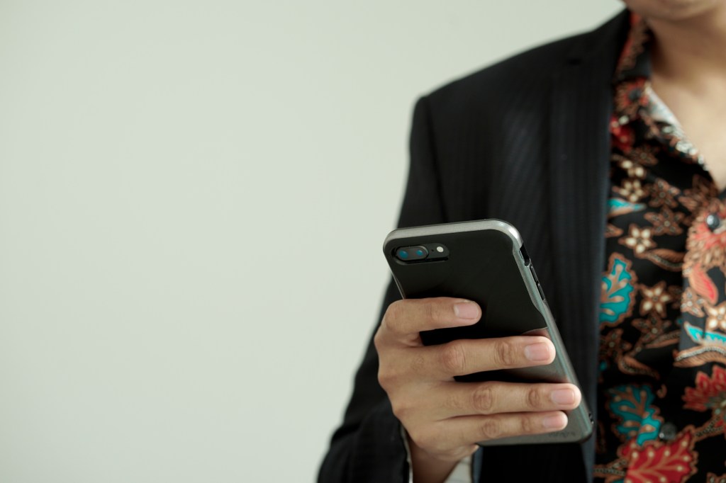 Midsection Of Man Using Mobile Phone While Standing Against Wall, photo taken in Jakarta, Indonesia