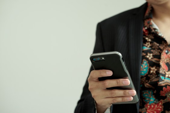 Midsection Of Man Using Mobile Phone While Standing Against Wall, photo taken in Jakarta, Indonesia