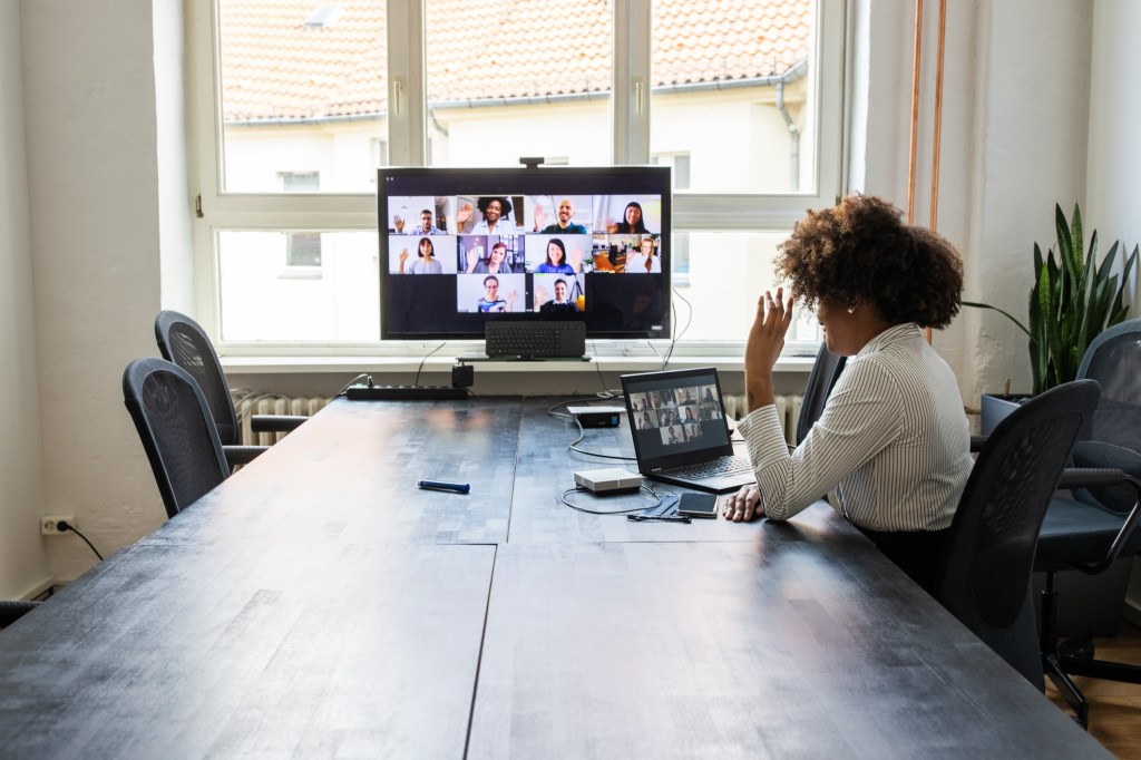 Rear view of a businesswoman having a meeting with team over a video conference in office board room. Meeting over a video call in office post pandemic lockdown.