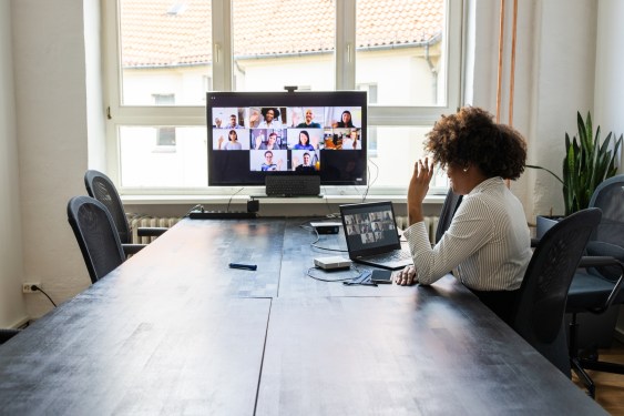 Rear view of a businesswoman having a meeting with team over a video conference in office board room. Meeting over a video call in office post pandemic lockdown.