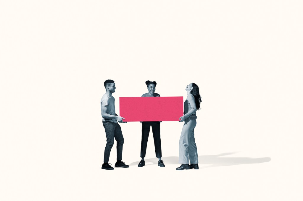 Full length of cheerful young friends carrying large pink block against white background