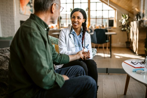Female mid adult doctor at home visit comforting patient, holding his hand
