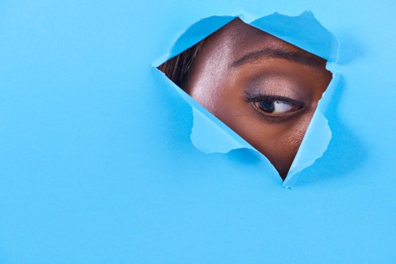 A view of a woman's eye looking through a hole in some colorful paper