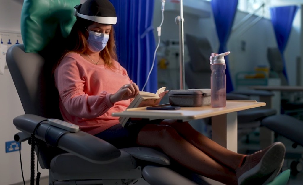 A woman sits in a chemotherapy clinic in a chair with Luminate's headset on.