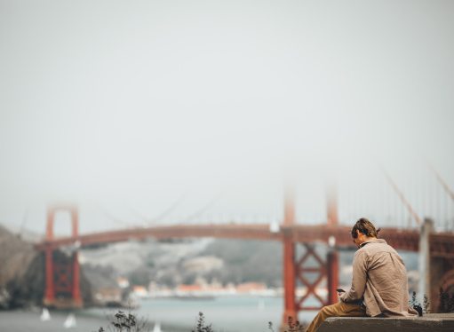 A person sits on Baker Beach in San Francisco with the Golden Gate Bridge in the background partially obscured by fog.