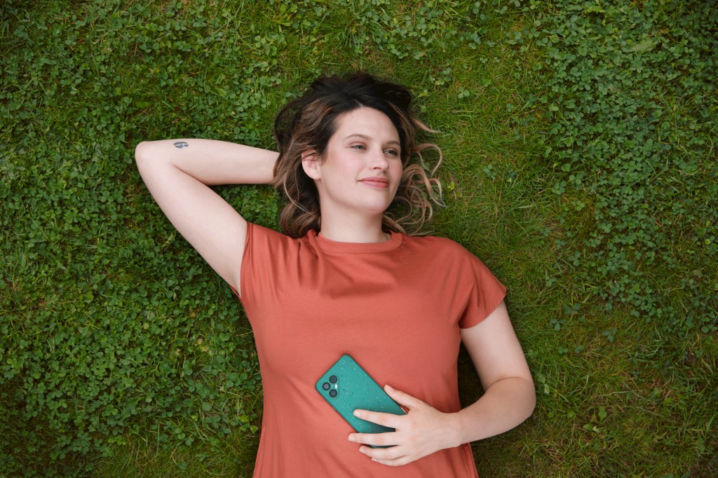 Woman holding mobile phone lying on back in grass