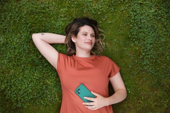 Woman holding mobile phone lying on back in grass
