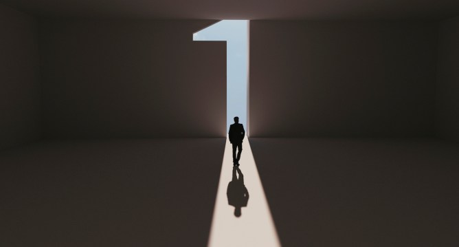 Man walks towards a big number one symbol that lights up. He is surrounded by darkness, but walks on a path of sunshine reaching first place. Note: Digitally generated image.