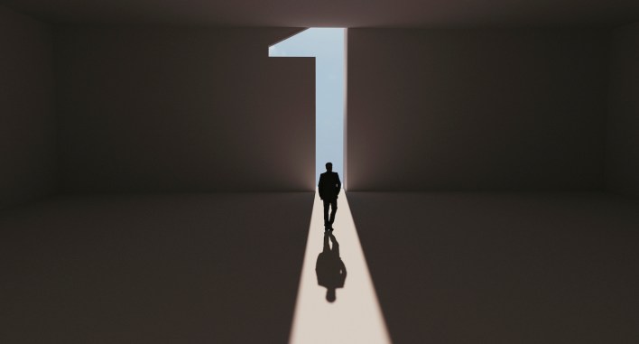 Man walks towards a big number one symbol that lights up. He is surrounded by darkness, but walks on a path of sunshine reaching first place. Note: Digitally generated image.