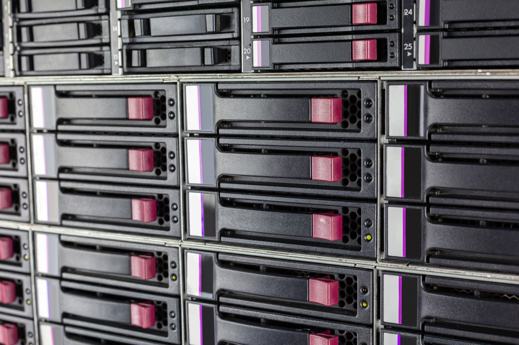 Array of hard drives in a computer data center server rack with plugs for LAN cables above in a close up detailed full frame view in a cloud computing concept