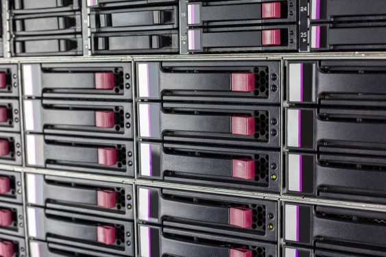 Array of hard drives in a computer data center server rack with plugs for LAN cables above in a close up detailed full frame view in a cloud computing concept
